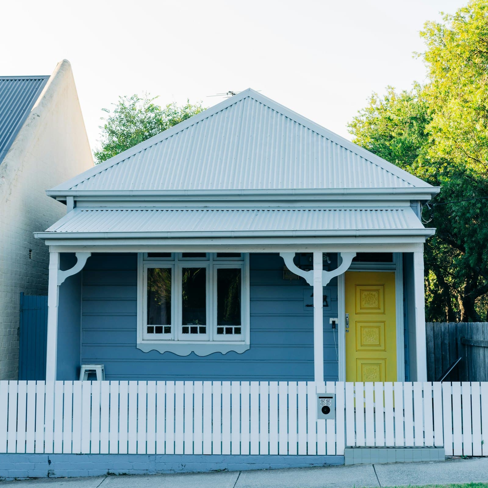 A weatherboard Federation-style cottage with a corrugated iron roof and decorative verandah, behind a white picket fence.